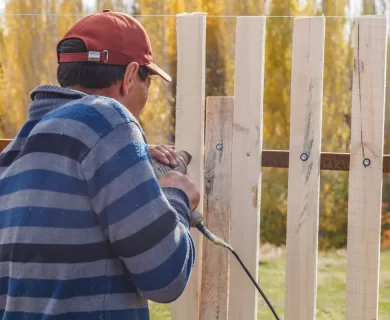 A man uses a drill to tighten a screw while installing a picket fence, showcasing fence maintenance.
