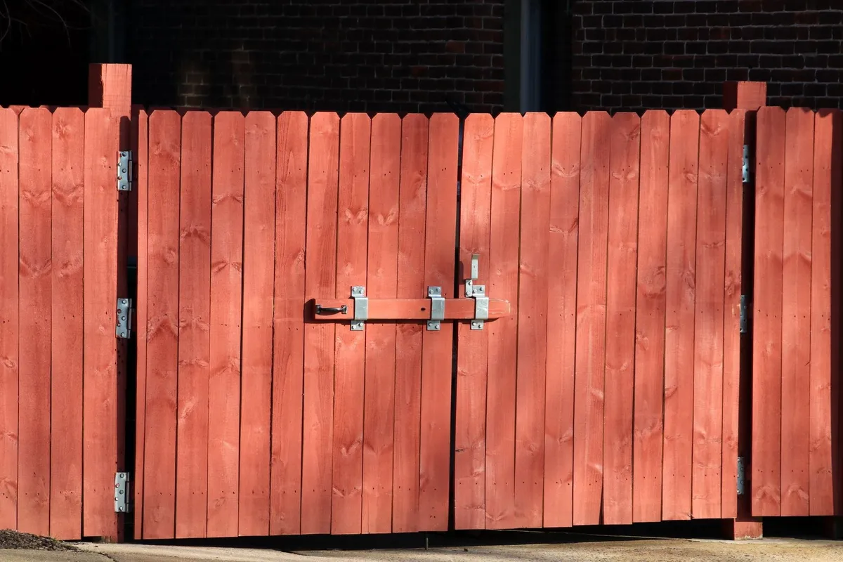 A rustic red wooden fence with a metal latch, symbolizing safety for DIY fence repair projects.