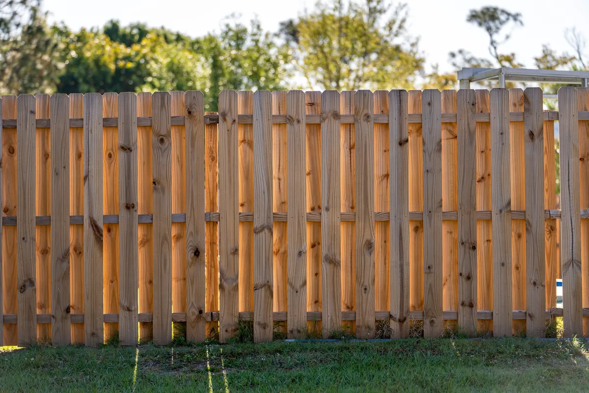 Wooden picket fence surrounding a green lawn, highlighting the importance of fence maintenance for privacy.