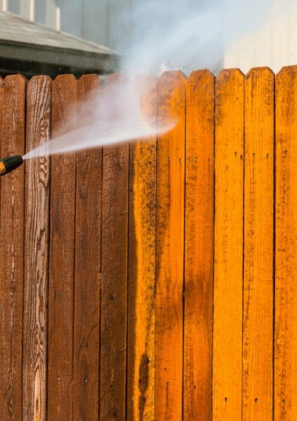 A contractor is pressure washing a wooden fence